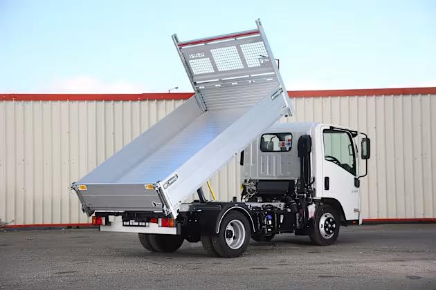Rear three-quarter view of Isuzu tipper truck with raised tipping bed in an industrial setting.