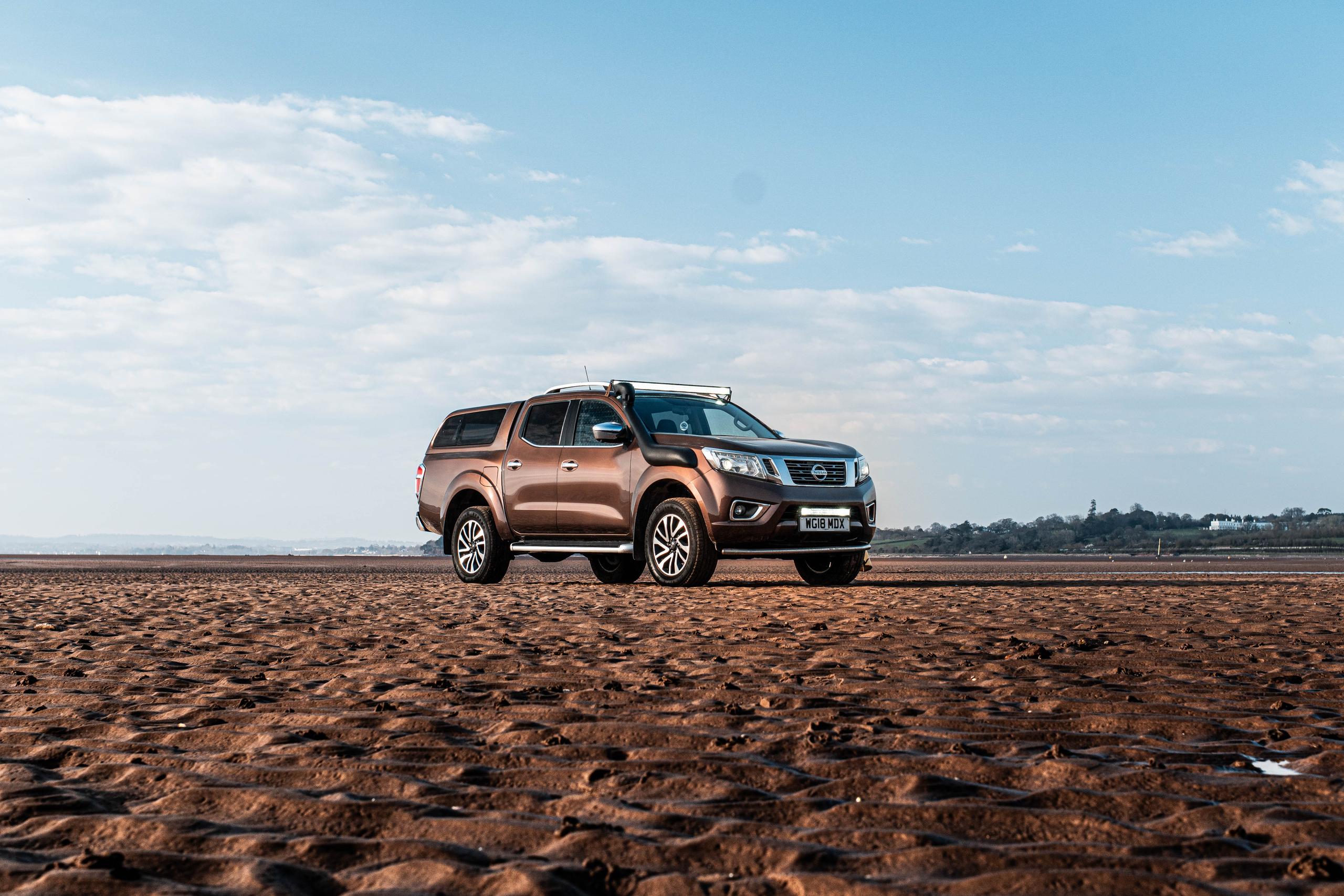 brown nissan navara parked on sandy beach