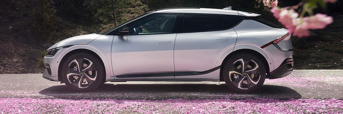 A side view of a white Kia EV6, with tree blossom in the foreground and flower petals on the ground