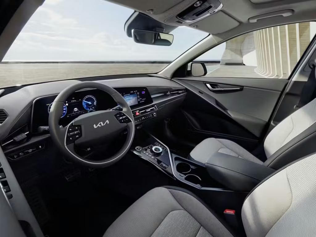 Interior view of the Kia Niro, featuring a dual-tone grey and black cabin with curved digital display, two-spoke steering wheel and sculptured centre console with rotary gear selector.