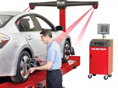 Technician performing a wheel alignment using Hunter equipment on a car in a garage setting.