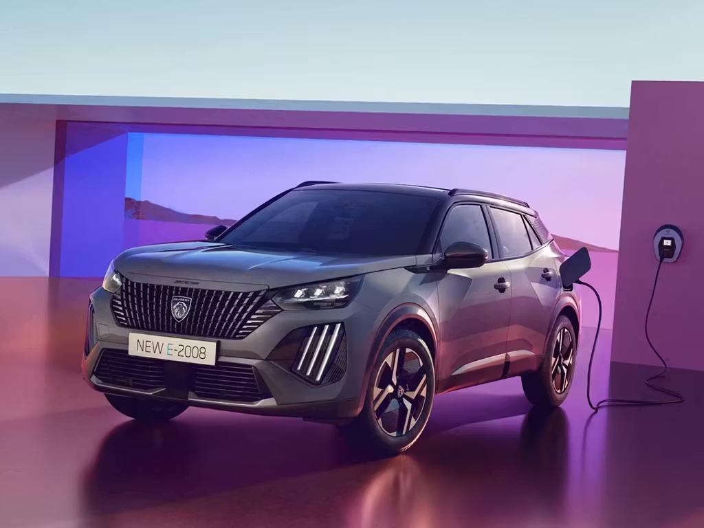 Peugeot E-2008 electric SUV charging at a wall-mounted charging point, showcasing its distinctive front grille, LED lighting signature and practical electric vehicle technology.