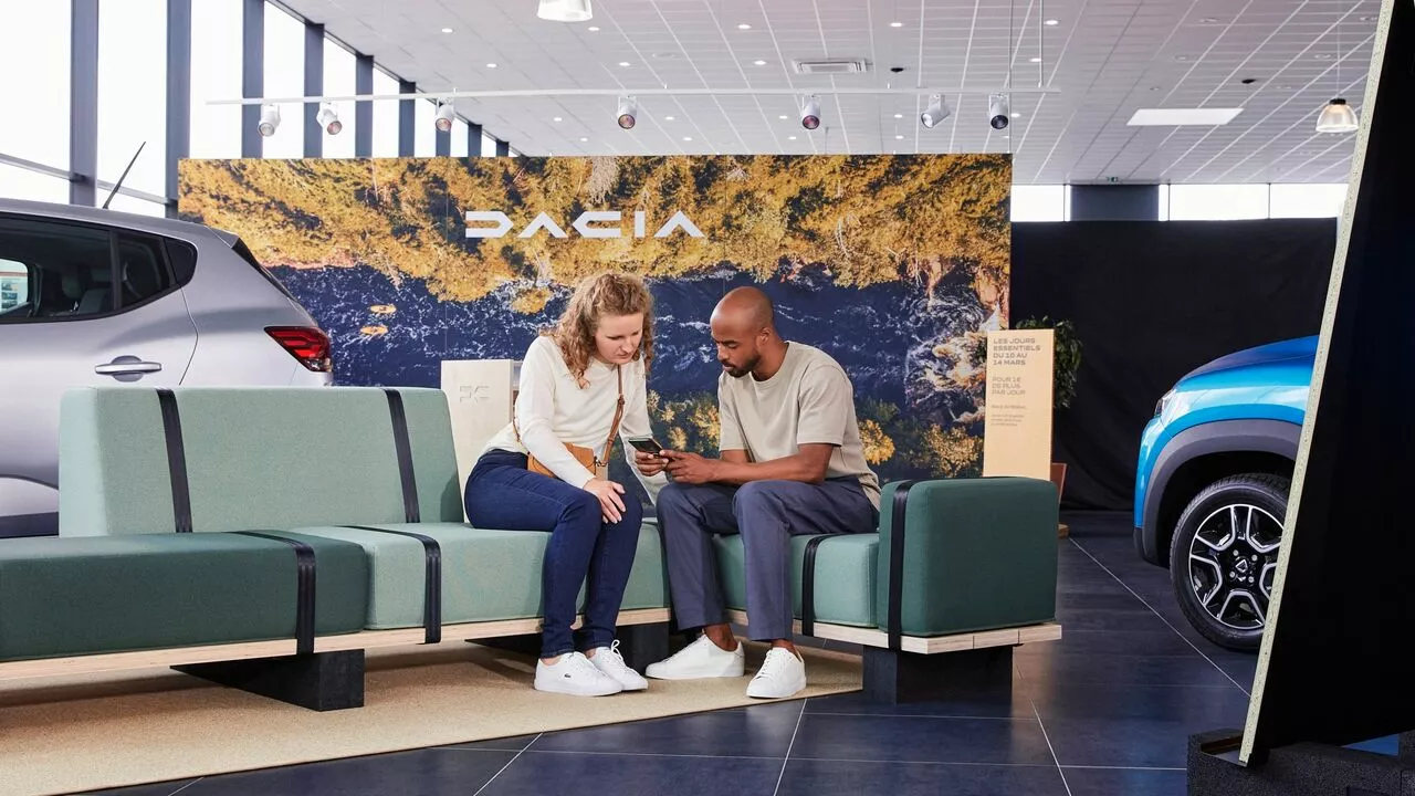 Two people reviewing Dacia servicing options on a phone inside the dealership.