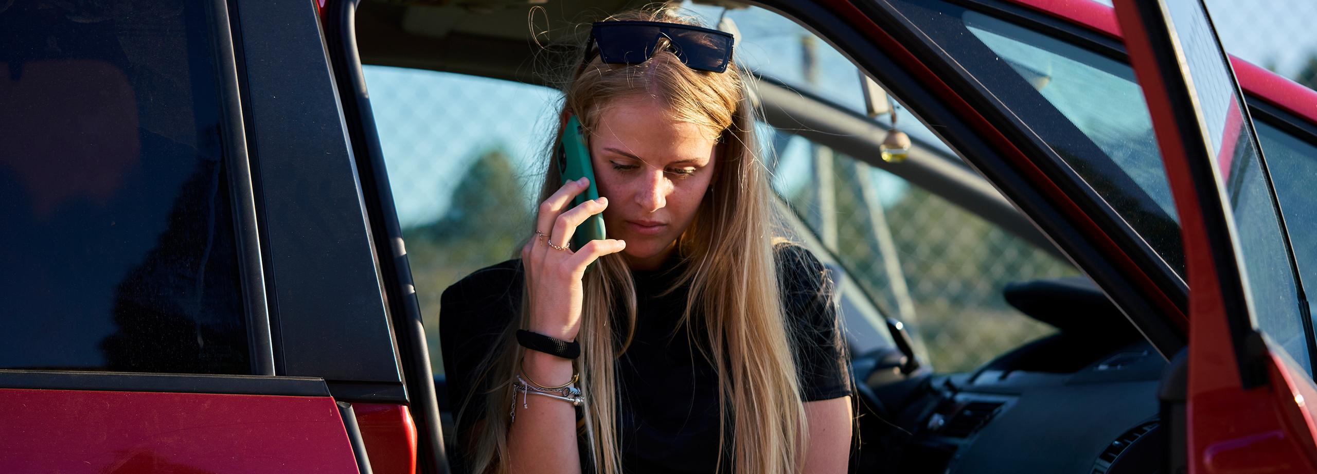 A woman sat in the driver's seat of a Nissan car, on the phone to insurance