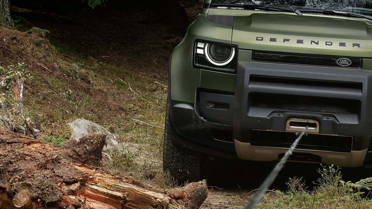 Front view of a Defender 130 using a winch while navigating a rocky forest trail.