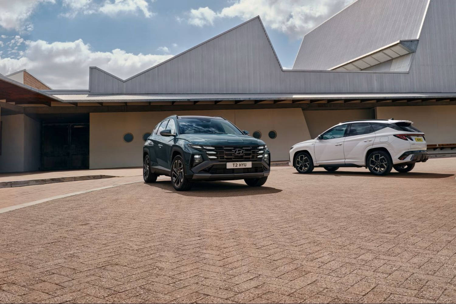 Two Hyundai Tucson models parked in front of a modern house
