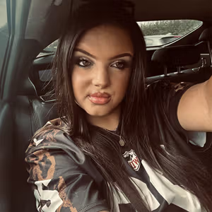 Portrait of a person in a vehicle wearing a patterned top and looking towards the camera.