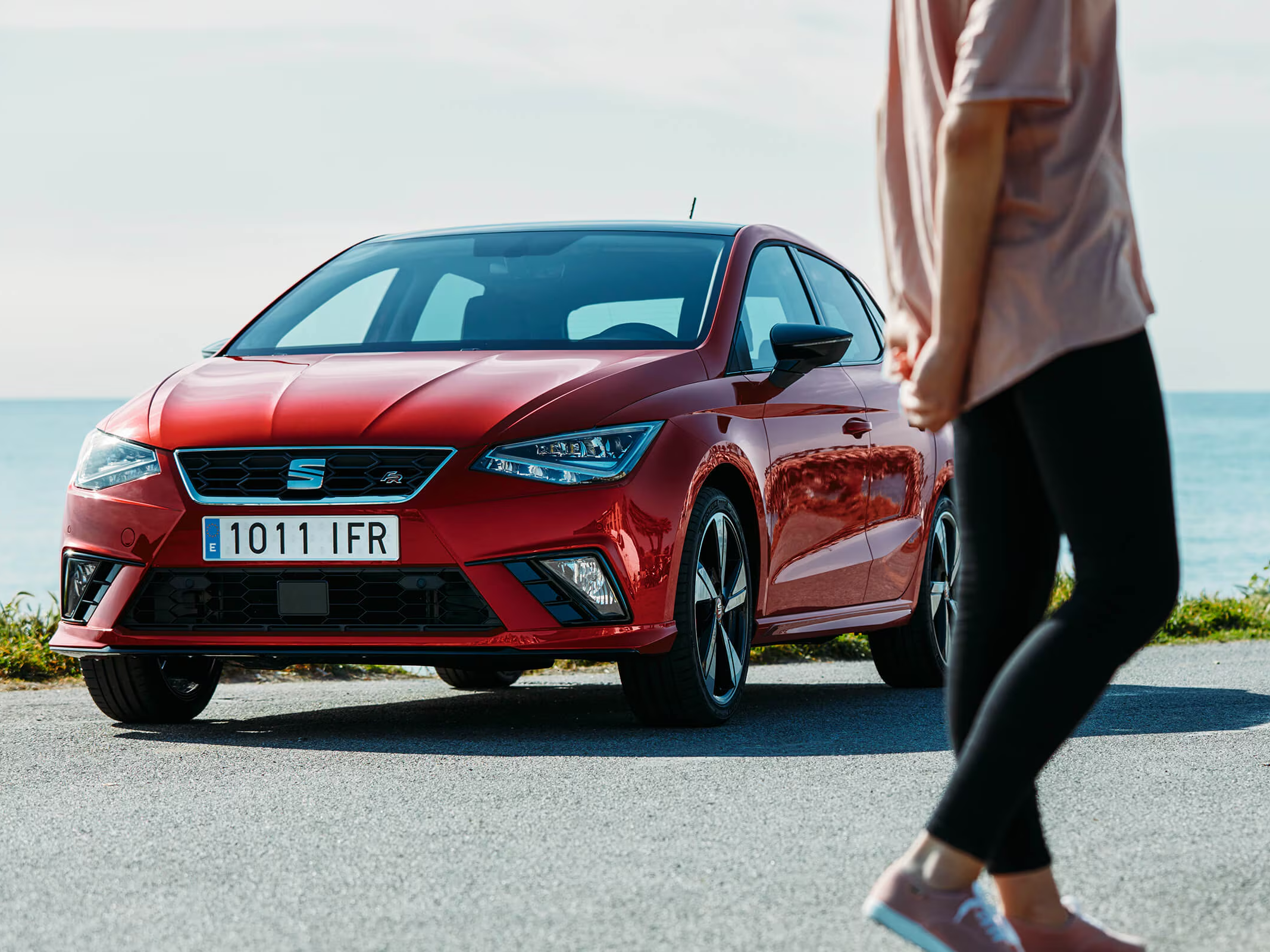 Red SEAT Ibiza parked by the seafront, with a person walking past in the foreground.