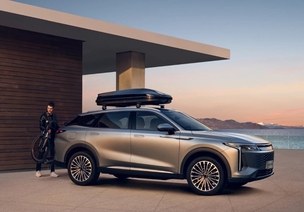 OMODA 9 parked outside a modern house with a roof cargo box, as a man stands beside it holding a bicycle.