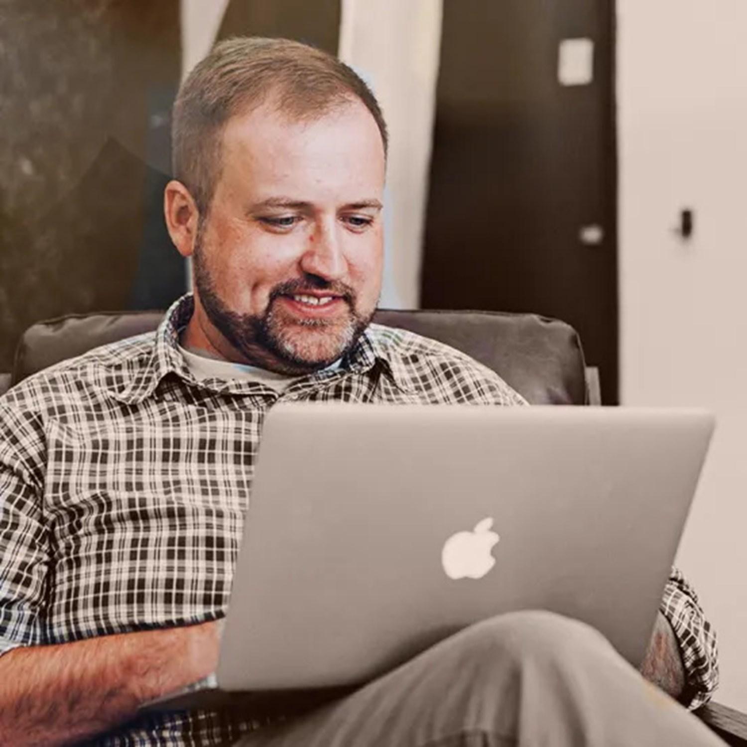 man smiling looking at apple laptop sat down 