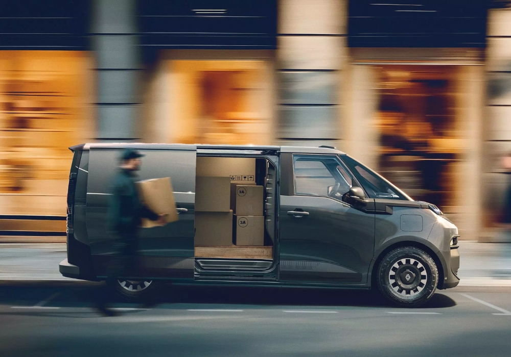 Side view of Renault Trafic E-Tech Electric van in motion with sliding door open, showing cargo area with boxes and a worker carrying a package.