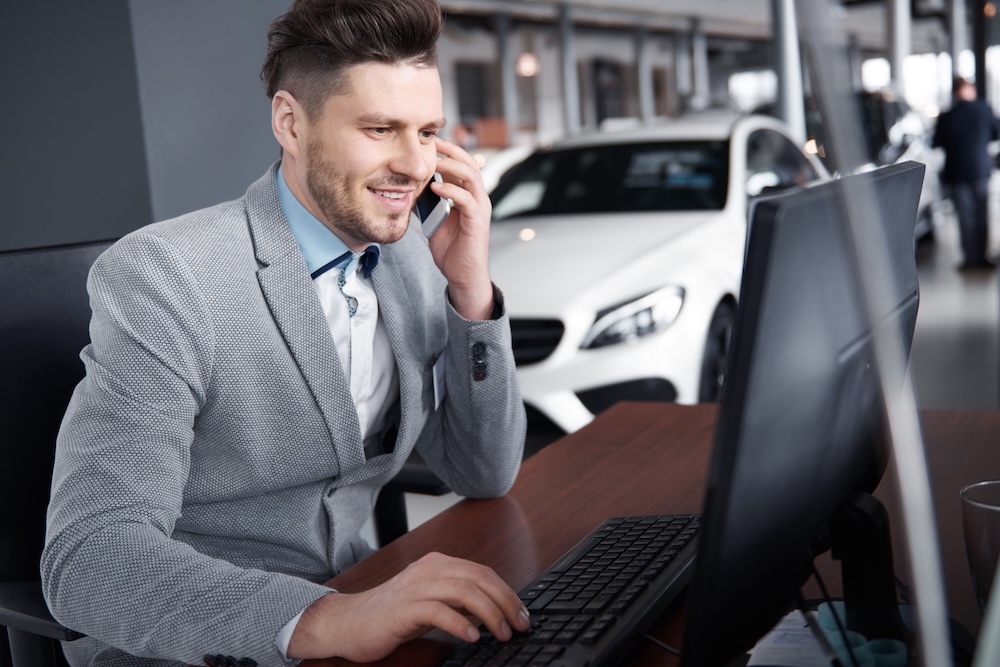 Man viewing a car on a laptop in a car dealership.