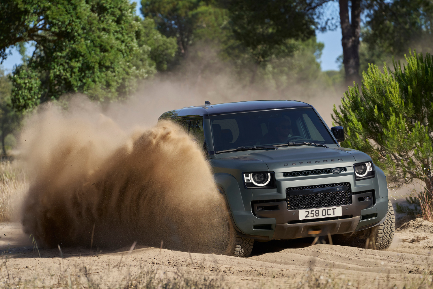 Land Rover Defender 110 driving off-road through sand and dust.