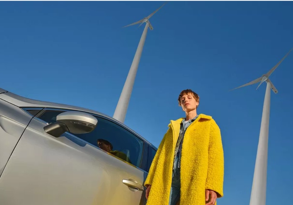 Low-angle view of a person beside a Renault vehicle with wind turbines in the background, emphasising sustainable mobility context.