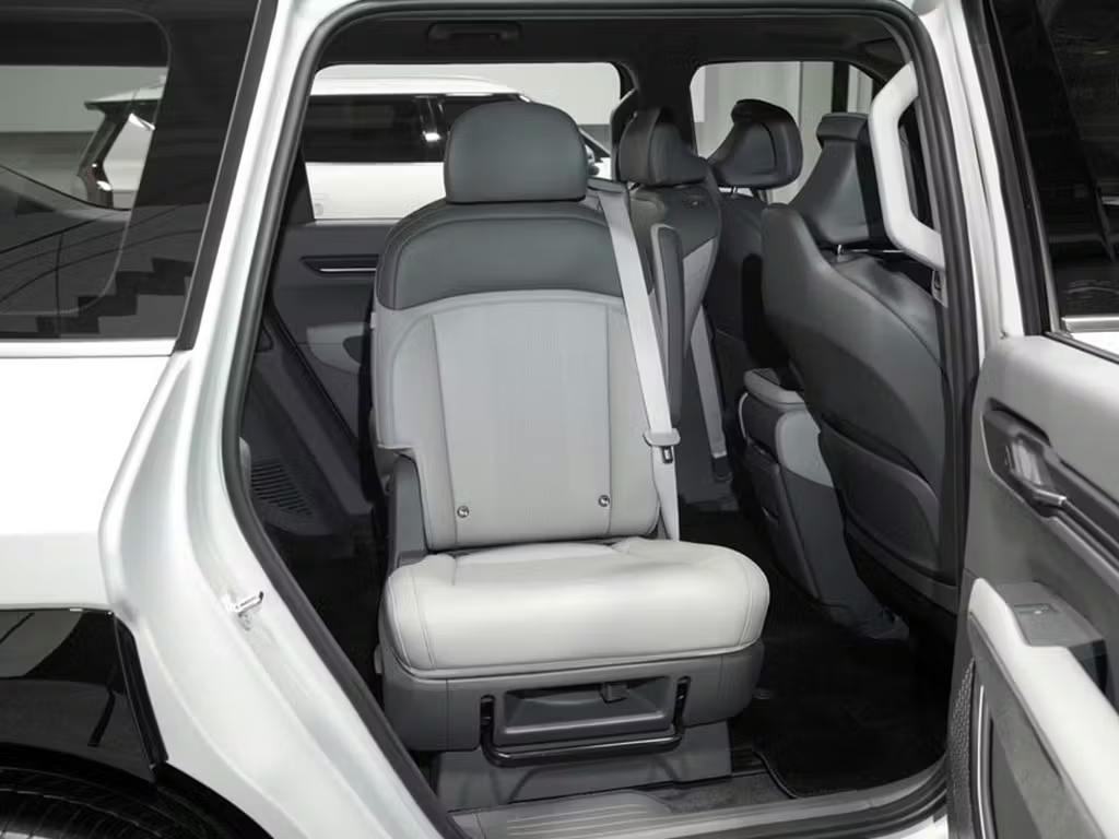 Interior view of the Kia EV9 seven-seater cabin through the open rear door, showcasing the grey leather third-row seating with integrated seatbelts and flexible seat configuration.
