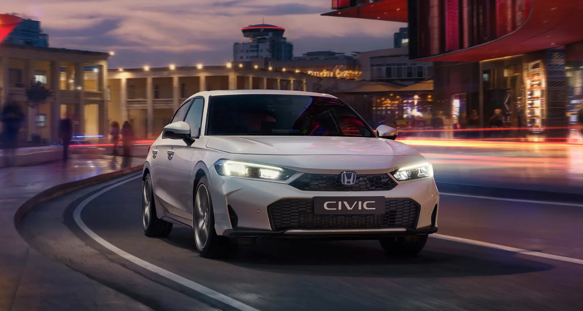 A silver Honda Civic driving along a street lit by neon lighting at night.