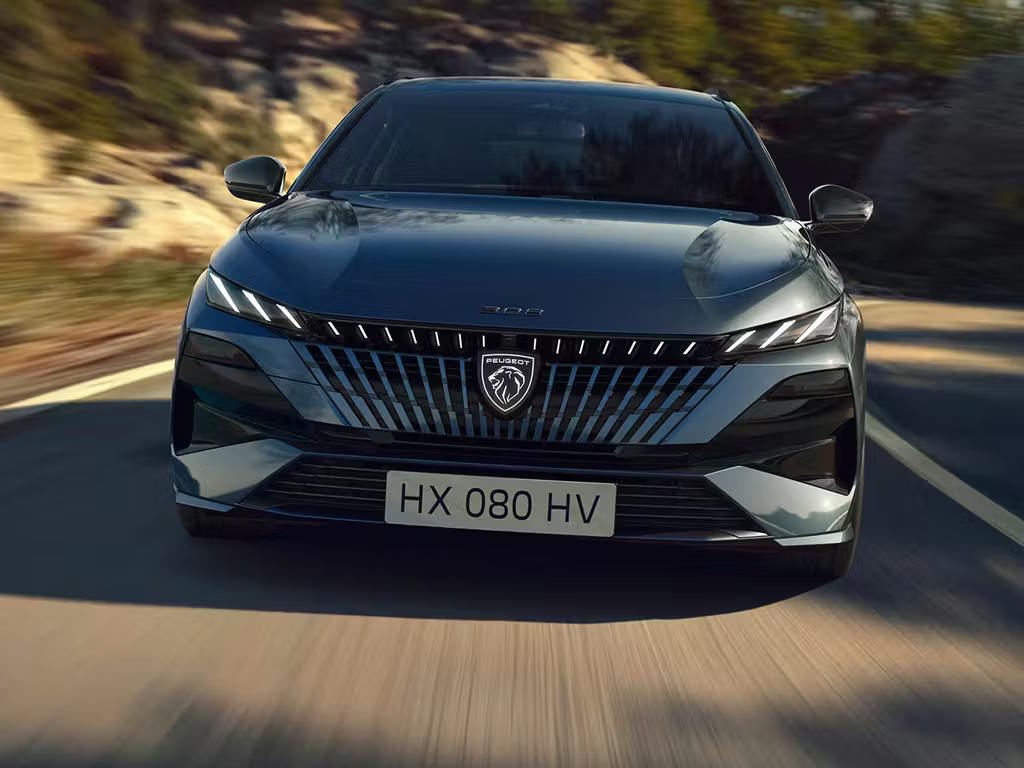 Front view of the Peugeot 308 SW estate in motion, featuring the bold frameless grille, distinctive fang-shaped LED daytime running lights and sculpted bonnet lines.