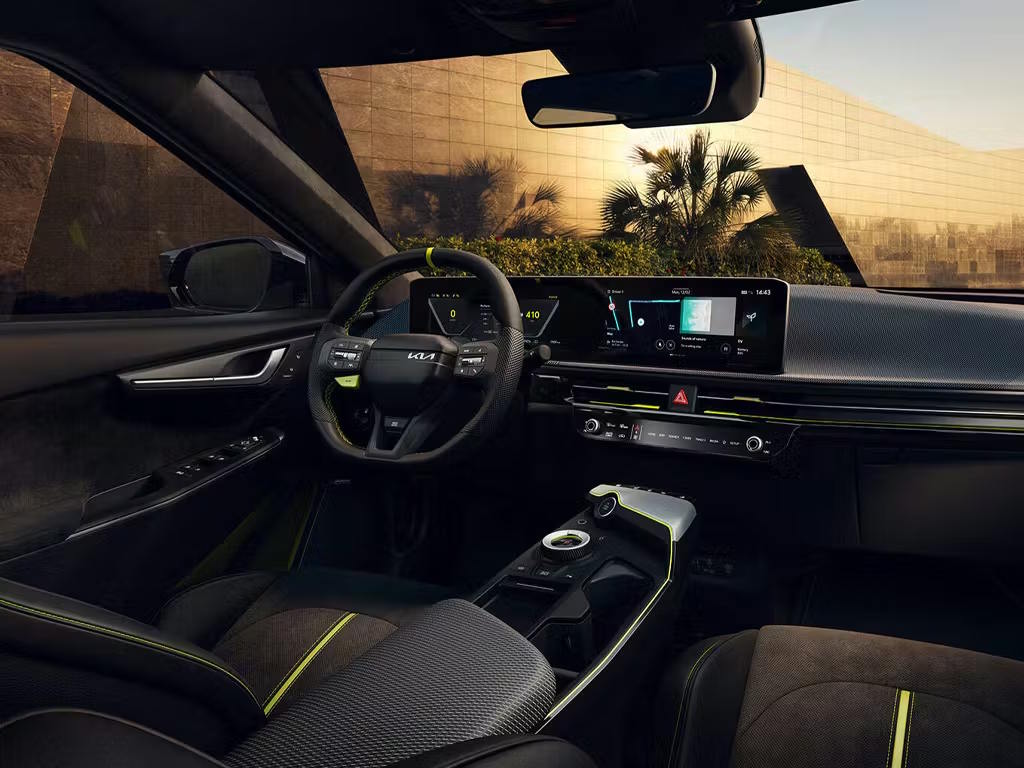 Interior view of the Kia EV6 GT, featuring the dual curved display screens, flat-bottomed steering wheel and sporty black upholstery with vibrant yellow-green contrast stitching accents.