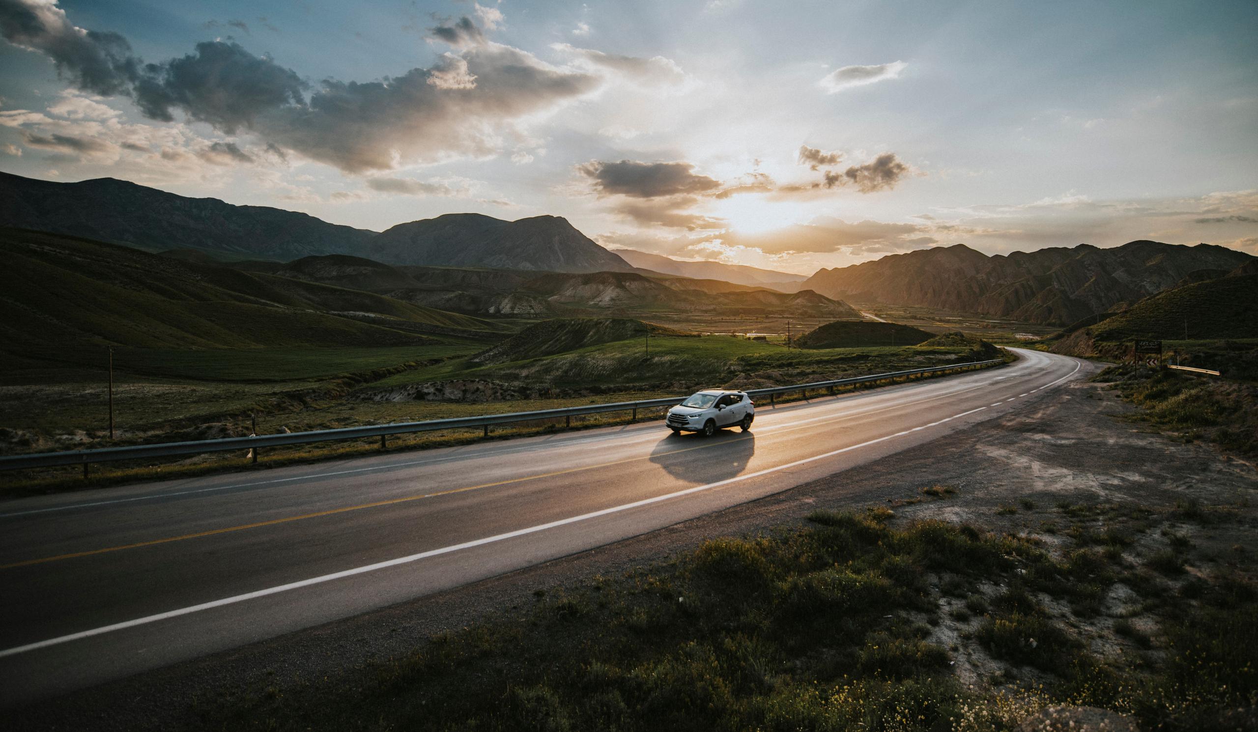 A white car driving in a scenic outdoor environment with mountains in the background.