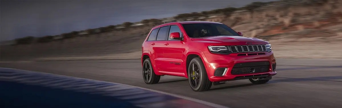 Red Jeep Grand Cherokee Trackhawk driving along road
