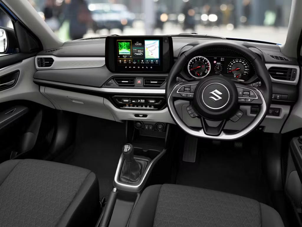 Interior view of the Suzuki Swift cabin, featuring a floating touchscreen infotainment display with navigation, analogue instrument cluster, multifunction steering wheel and dark cloth upholstery.