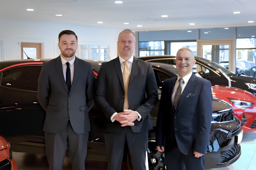 Dealership team standing together in the showroom beside new vehicles.