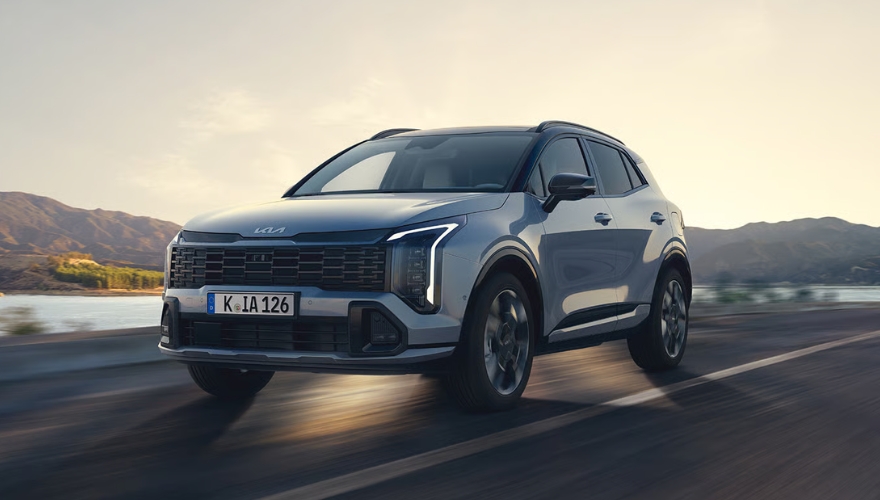 Silver Kia Sportage driving along a scenic lakeside road.