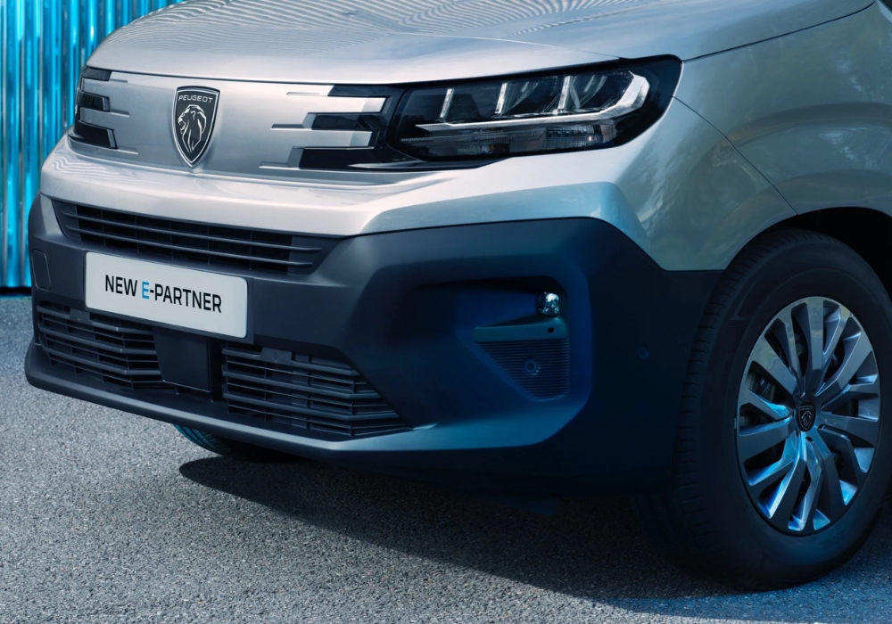 Peugeot e-Partner front bumper and grille detail with alloy wheel visible in an industrial setting.