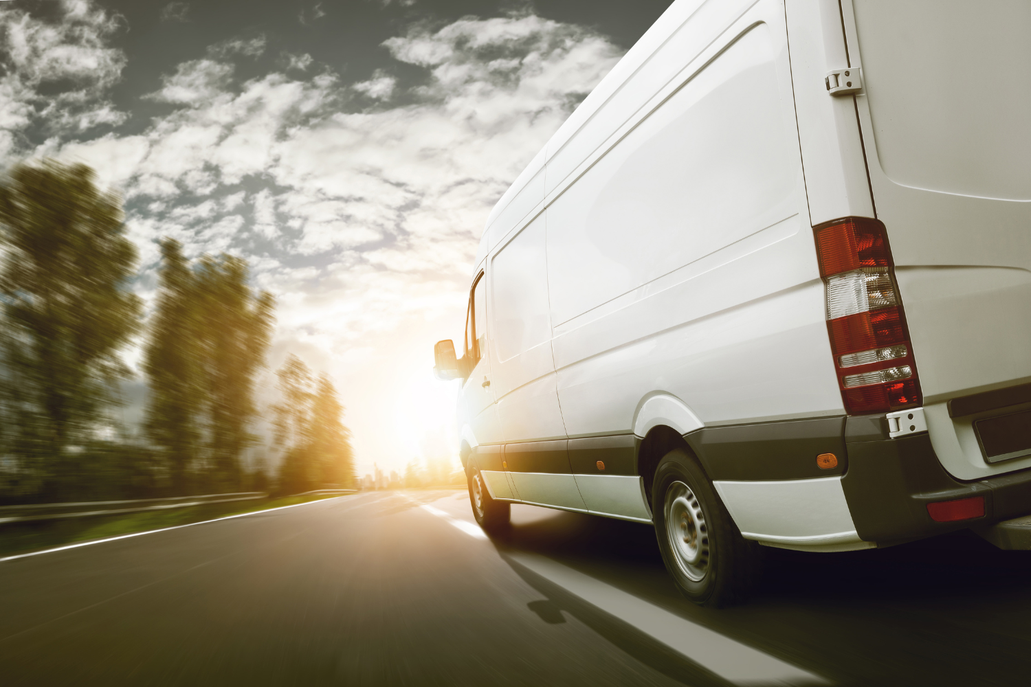 White delivery van driving along a road at sunset.