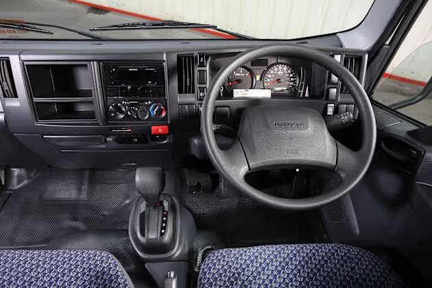 Interior dashboard and steering wheel of an Isuzu Grafter truck, showing the driver controls, gear selector, and instrument panel.