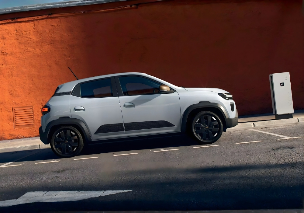 Dacia Spring parked along a street beside a charging station, highlighting convenient electric charging in an urban setting.