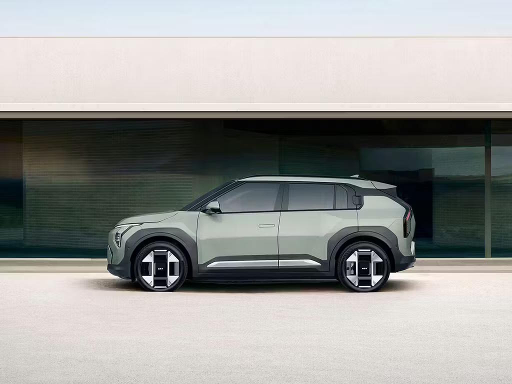 Side profile view of the Kia EV3 compact electric SUV in sage green, featuring bold geometric alloy wheels, a distinctive C-pillar design and a boxy yet modern silhouette.