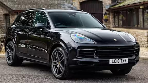 Black Porsche Cayenne SUV parked in front of stone buildings, shown from the front three‑quarter view.