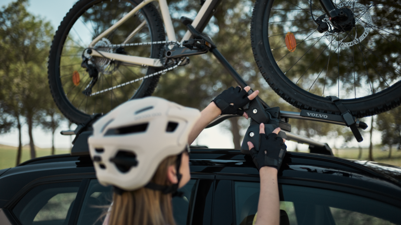 Cyclist securing bicycle to Volvo roof-mounted bike rack.