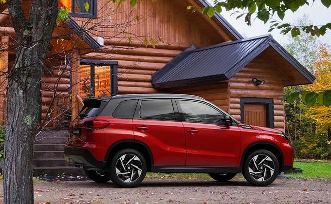 Red Suzuki Vitara parked beside a wooden cabin.