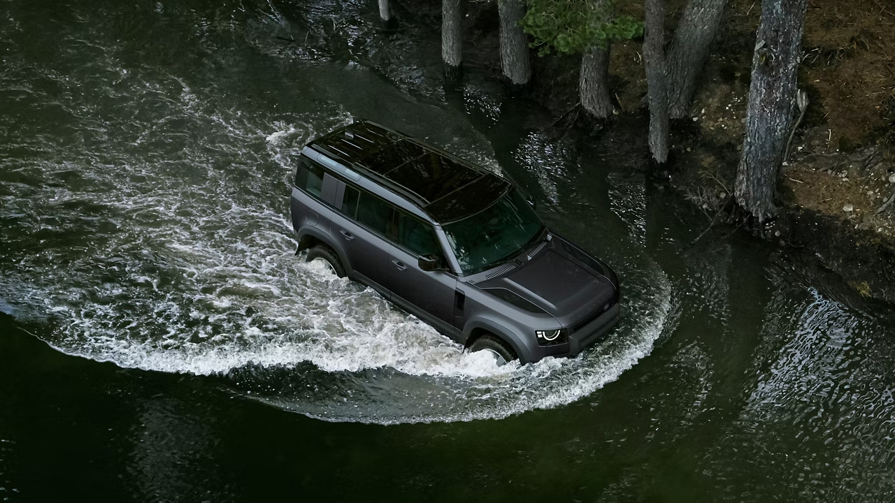 Defender 110 driving through deep water in a forest environment.