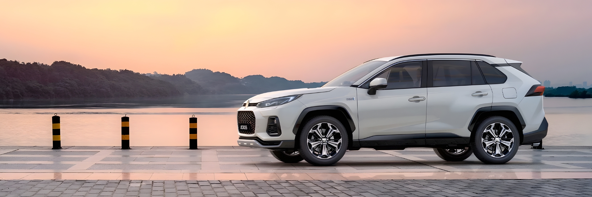 White Suzuki Across parked beside a lakeside walkway at sunset.