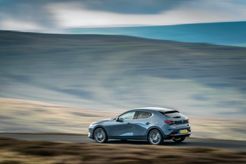 A grey Mazda3 car driving along a country road at speed.