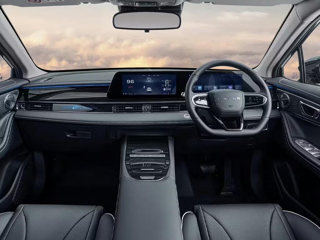 Interior cabin view of the OMODA 5 SHS, featuring a dual-screen digital dashboard, leather-wrapped steering wheel, dark grey upholstery and ambient lighting accents.