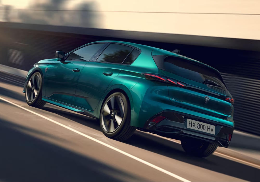 Peugeot 308 hatchback in green shown from rear three-quarter angle driving along a city road.