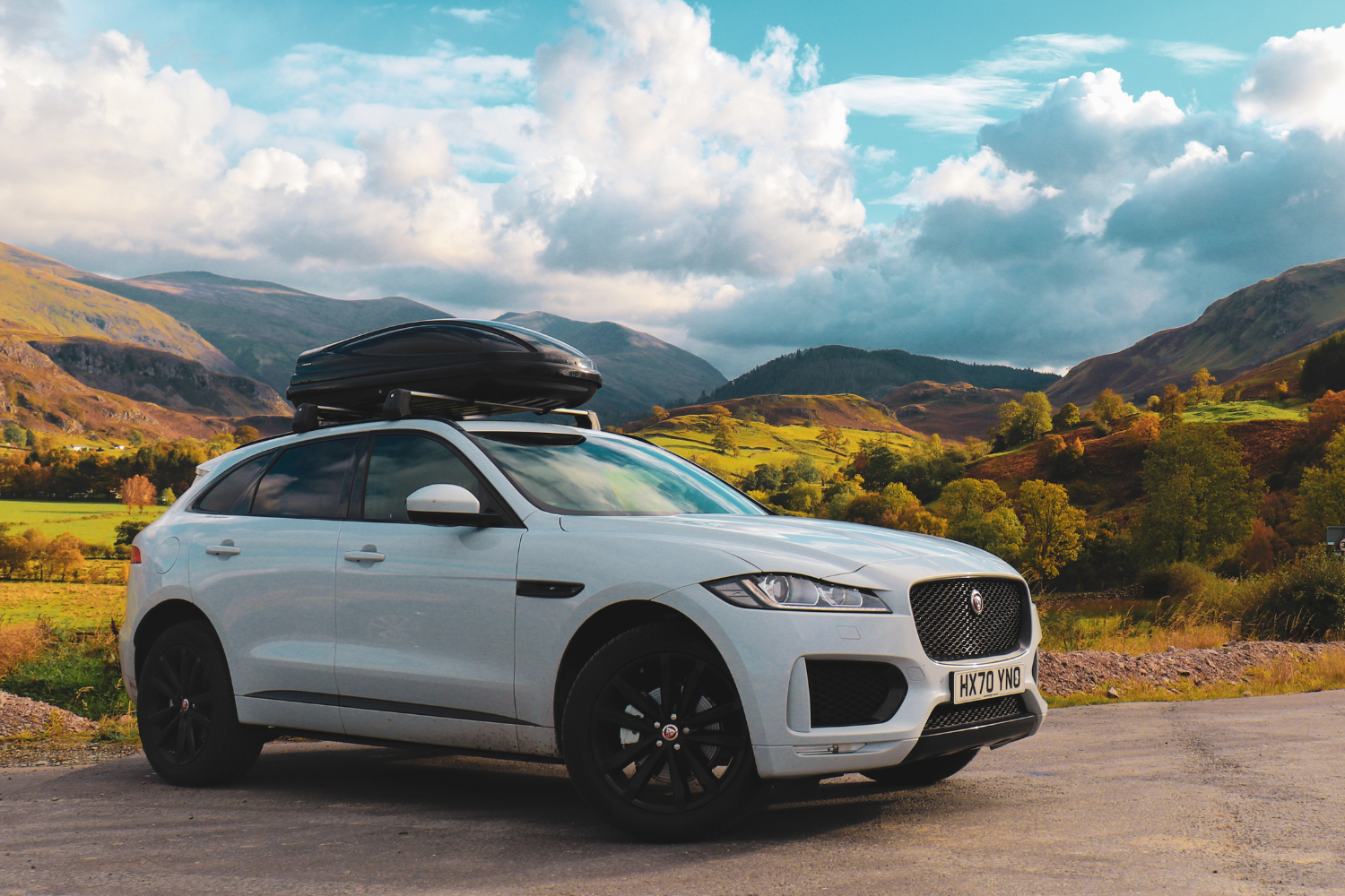 Jaguar F-PACE with roof box in scenic countryside.