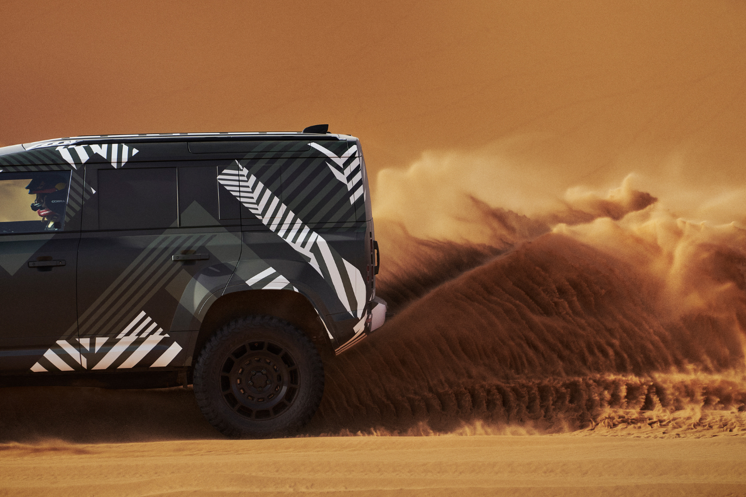 Land Rover Defender powering through desert sand dunes.