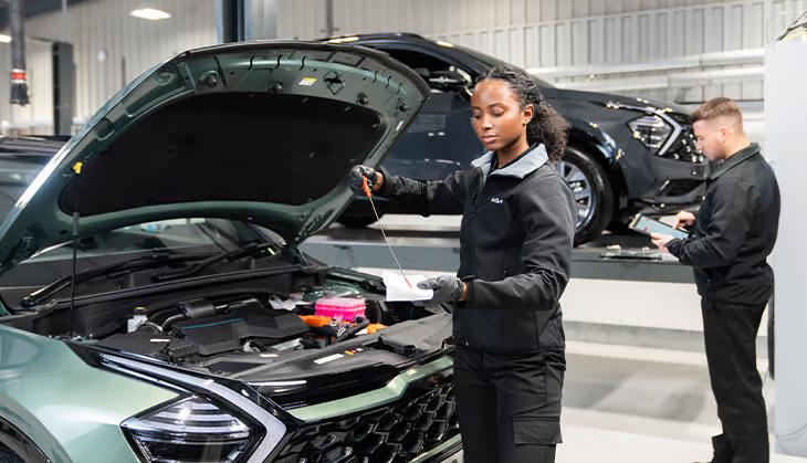 Kia technicians carrying out a vehicle inspection and maintenance check in a professional workshop environment.