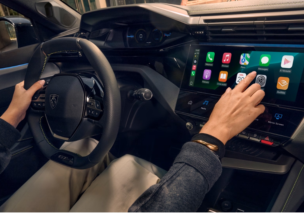 Peugeot 308 interior with driver using central touchscreen infotainment system and app interface.