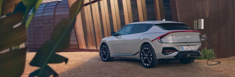White Kia EV6 connected to a home charging station outside a modern house.