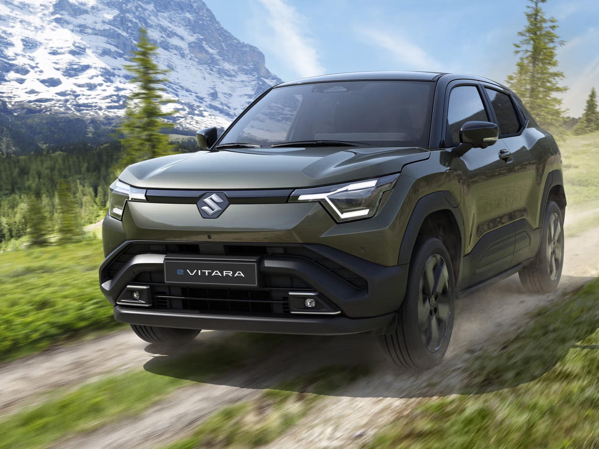 Front three-quarter view of the Suzuki eVitara electric SUV in khaki green, tackling a mountain trail with angular LED headlights and rugged black cladding on display.