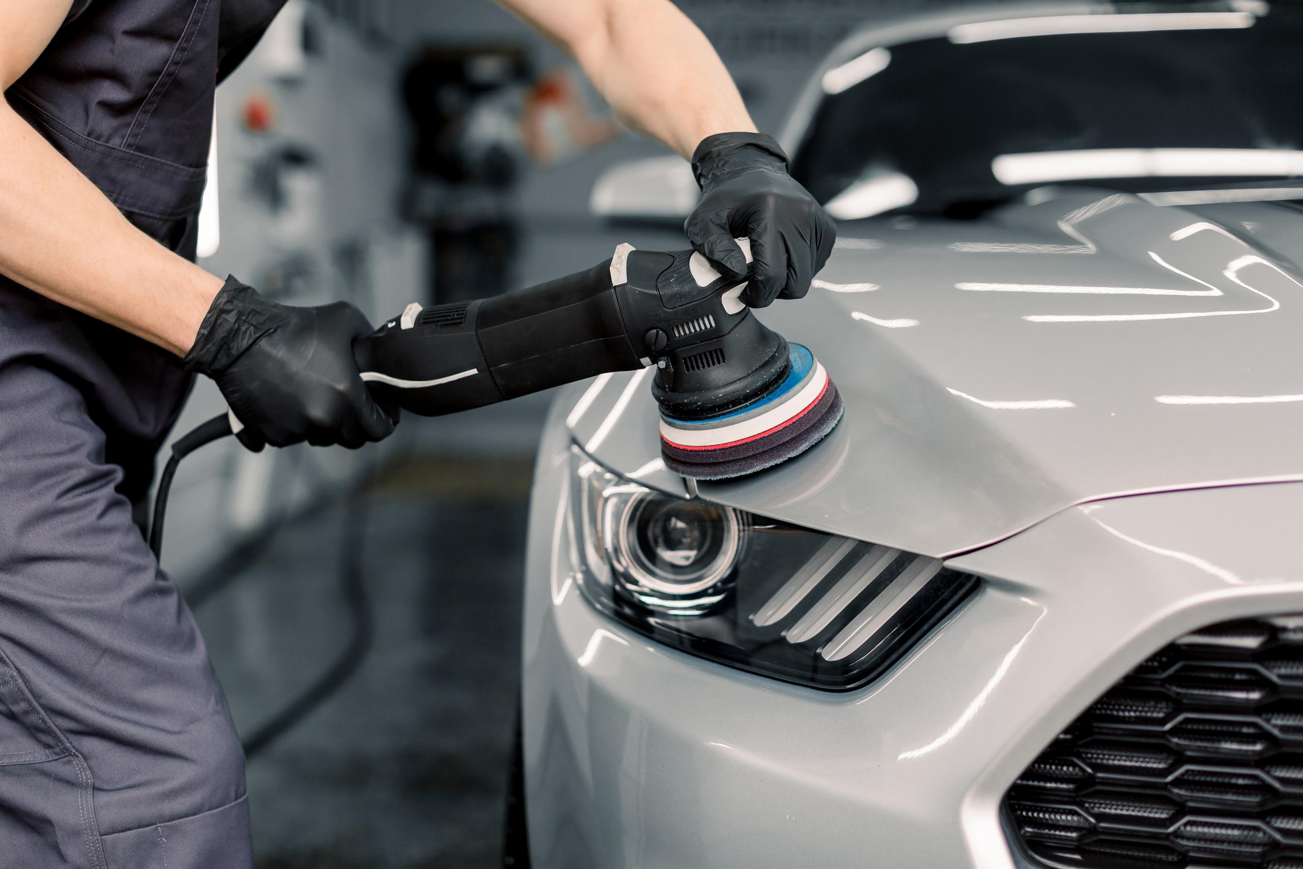 Technician using a machine polisher on the front of a white car.