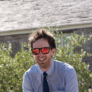 Outdoor portrait of a person laughing in a garden setting while wearing reflective sunglasses.