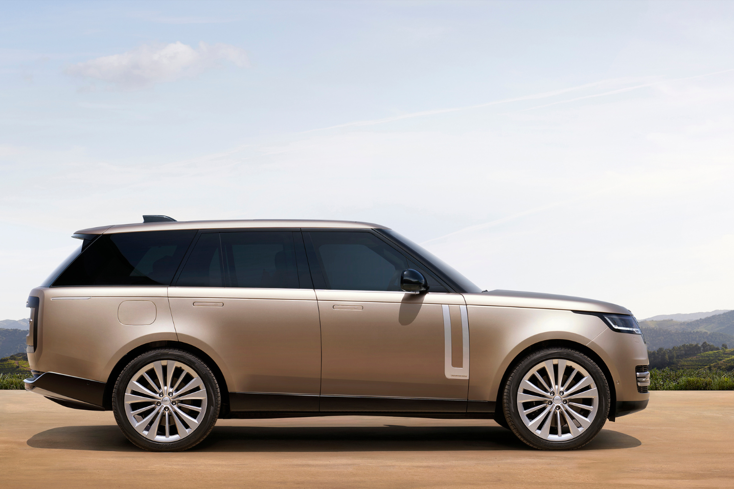 Gold Range Rover parked with countryside backdrop.