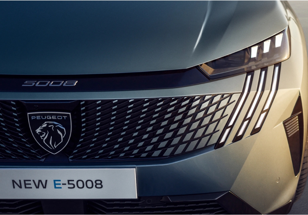 Close-up of Peugeot E-5008 front grille, badge, and distinctive LED daytime running lights.
